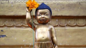 A devotee (unseen) sprinkles rice grains as part of the rituals on the idol of Buddha, at Swayambhu in Kathmandu. Devotees visit temples, light candles and incense sticks, pray and offer sweets and fruits before the statue of Lord Buddha