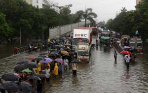 People walk through flooded roads as vehicles are seen stuck in a traffic jam due to heavy rains in Mumbai on June 19, 2015
