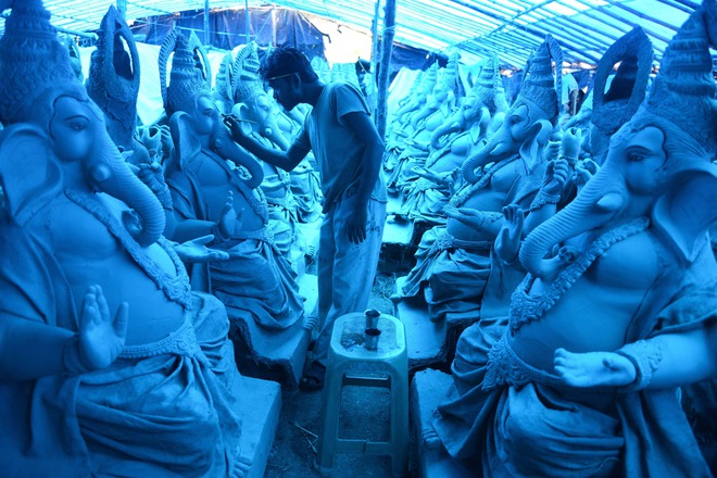 An Indian artist works on eco-friendly figures of Hindu God Lord Ganesh made with mud, jute and bamboo at a blue tarp-covered workshop on the outskirts of Hyderabad on September 15, 2015. The statues of eco-friendly clay Ganesh idols made with mud, jute and bamboo will reduce pollution during the Ganesh immersion