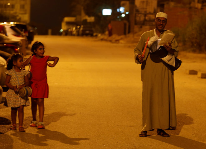 Girls look on and listen to their names as El Mesaharty, Hussien, 40, wakes up residents for their pre-dawn meals during the first day of Ramadan in Cairo, Egypt June 6.