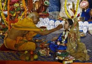 A Hindu priest (L) offers sweets to a five-and half-year old girl dressed as a Kumari at a pandal or temporary platform during the religious festival of Durga Puja in Kolkata on October 21, 2015. Kumari is a young virgin girl who is worshipped as part of the Durga Puja rituals.
