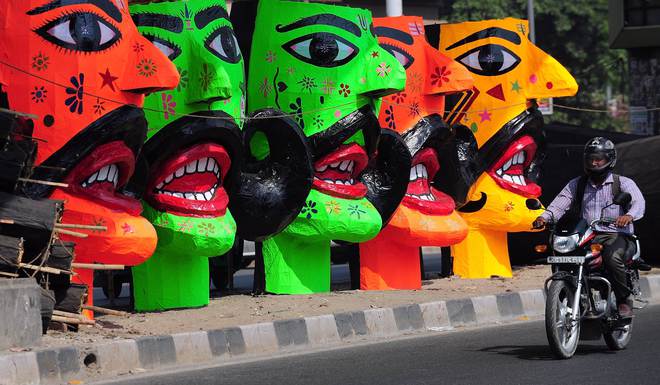 An motorcyclist passes by the effigies of the demon king of Hindu Mythology, Ravana, displayed for sale at a roadside in New Delhi on October 20, 2015