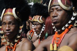 Naga tribe members look on as others perform on the third day of the annual Hornbill Festival at Kisama, some 15 km from Kohima, Nagaland, on December 3, 2016.