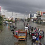 People stand on a flooded road in Chennai on December 2, 2015. The heaviest rainfall in over a century caused massive flooding across the Indian state of Tamil Nadu, driving thousands from their homes, shutting auto factories and paralysing the airport in the state capital Chennai.