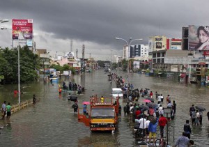 People stand on a flooded road in Chennai on December 2, 2015. The heaviest rainfall in over a century caused massive flooding across the Indian state of Tamil Nadu, driving thousands from their homes, shutting auto factories and paralysing the airport in the state capital Chennai.