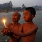 A Hindu man and his son hold burning incense sticks and a candle as they pray after taking a dip in the waters of river Howrah on the occasion of Makar Sankranti in Chakmaghat village, Tripura, on January 14, 2017