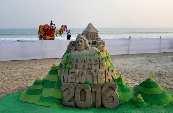 A boy enjoys camel ride on the back drop of a New Year sand sculpture created by sand artist Manas Sahoo on the eve of New Year at Puri beach