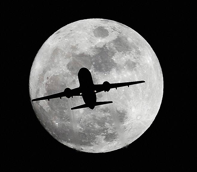 An airplane crosses a nearly full moon on its way to Los Angeles International Airport near Whittier, California, on December 24, 2015