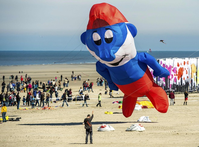 People fly a kite in the shape of comic strip character Papa Smurf during the 30th International Kite Festival in Berck-sur-Mer in northern France on April 12, 2016