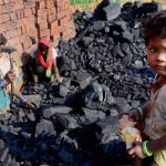 Allahabad: A child reacts to camera as her mother breaks coal at a brick factory in Allahabad on International Women's Day