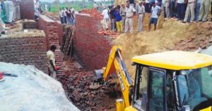 A JCB machine removes the debris after a wall of a stone crusher under construction collapsed in Mahendergarhs Dhelera Village