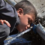 A Pakistani child drinks water from a pipe in a makeshift settlement in Peshawar