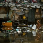 A man on a makeshift raft searches for discarded plastic bottles over a polluted river in Manila