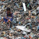 A young Indian child sits among piles of garbage at a dumping site in Dimapur on April 22, 2016, on World Earth Day.