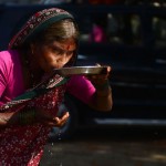 An Indian woman drinks water by a plate in Allahabad