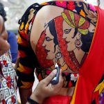 An artist applies final touches to a tattoo sketched on the back of a woman in preparations for the upcoming Navratri, a festival when devotees worship the Hindu goddess Durga and youths dance in traditional costumes in Ahmedabad, India, on September 26, 2016.