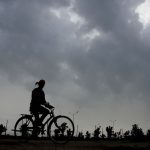 A cyclist rides past as pre-monsoon clouds loom over Karnal’s sky