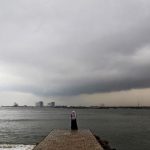 A woman stands on a seaside promenade against the background of pre-monsoon clouds gathered over the Arabian Sea in Kochi