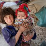 An internally-displaced Afghan girl holds a child at a refugee camp in Kabul, Afghanistan, on May 31, 2016.