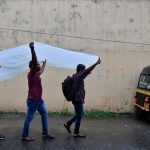 Men use a plastic sheet to cover from rain as they walk along a road in Kochi