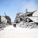 Syrian men ride a motorcycle past destroyed buildings in the rebel-held village of Teir Maalah, on the northern outskirts of Homs, on April 20, 2016.