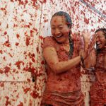 Two women enjoy as crowds of people throw tomatoes at each other, during the annual