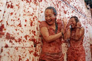 Two women enjoy as crowds of people throw tomatoes at each other, during the annual