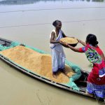 Women unload rice grains from a boat to dry in the sunshine in flood-affected village Murkata in Morigaon district in Assam.