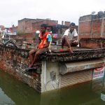 Men sit on the roof of a partially submerged shop in a flooded residential colony in Uttar Pradesh’s Allahabad on August 23, 2016