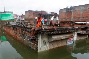 Men sit on the roof of a partially submerged shop in a flooded residential colony in Uttar Pradesh’s Allahabad on August 23, 2016