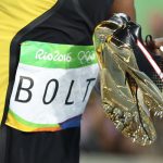 Usain Bolt carries his shoes in his hands after winning the gold medal.