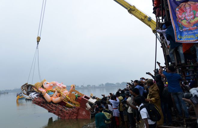 A devotee takes pictures as crane workers immerse a 58-foot idol of the Hindu god Ganesh in the Hussain Sagar Lake during the Ganesh Chaturthi festival in Hyderabad.