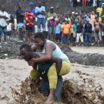 A man carries a woman across a river at Petit Goave where a bridge collapsed during the rains of the Hurricane Matthew, southwest of Port-au-Prince, on October 5, 2016.