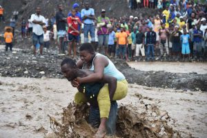 A man carries a woman across a river at Petit Goave where a bridge collapsed during the rains of the Hurricane Matthew, southwest of Port-au-Prince, on October 5, 2016.
