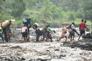 Haitian people cross the river La Digue in Petit Goave where the bridge collapsed during the rains of the Hurricane Matthew, southwest of Port-au-Prince, on October 5, 2016.