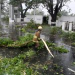 A rescue member removes a fallen branch of a tree that fell on a road after it was uprooted by strong winds in Chennai on December 12, 2016
