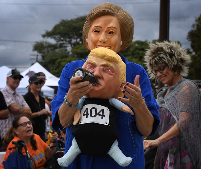 A woman wearing a Hillary Clinton mask carries a Republican presidential nominee Donald Trump doll during a Halloween parade in Long Beach, California on October 30, 2016.