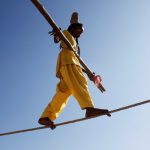 A tightrope walker performs on a rope while holding a balancing pole at Pushkar Fair.
