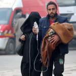 A man carries a child with an IV drip as he flees deeper into the remaining rebel-held areas of Aleppo, Syria, on December 12, 2016.
