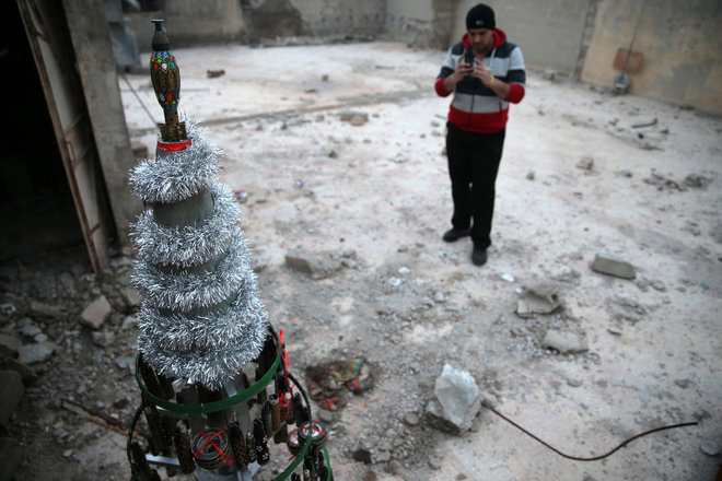 Akram Abu al-Foz takes a picture of a Christmas tree he decorated from empty shells which he collected and painted on, in the rebel held besieged city of Douma, in the eastern Damascus suburb of Ghouta, Syria December 23, 2016. Picture taken December 23, 2016.