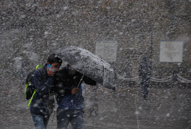 Pedestrians shelter under an umbrella as they walk through heavy snowfall on a road in Shimla on December 25, 2016