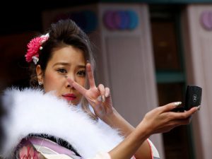 A Japanese woman wearing a kimono makes a V sign while she checks her make-up during the Coming of Age Day celebration ceremony at an amusement park in Tokyo, Japan