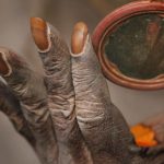 A Hindu holy man holds a mirror as he smears his body with ash and vermillion paste