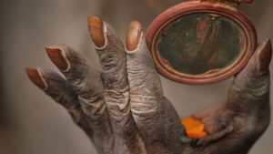 A Hindu holy man holds a mirror as he smears his body with ash and vermillion paste