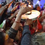 A lady holds up a thali with a burning flame to bless devotees
