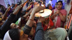 A lady holds up a thali with a burning flame to bless devotees