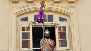 A man dressed in traditional attire watches the procession from his balcony in Girgaum