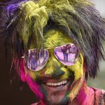 A man face covered with bright neon powder poses for a picture during Holi celebration