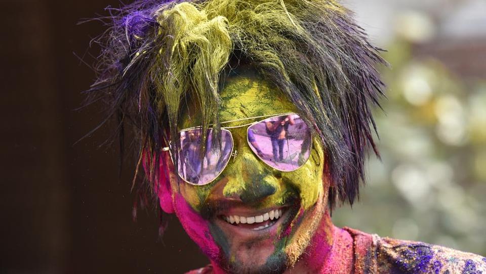 A man face covered with bright neon powder poses for a picture during Holi celebration