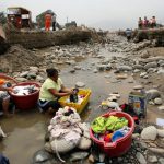 Residents do the laundry at a flooded Ramiro Priale highway, after rivers breached their banks due to torrential rains, causing flooding and widespread destruction in Huachipa, Lima, Peru